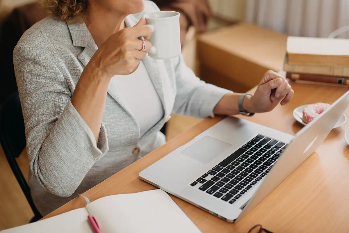 A woman with coffee working on a laptop at a bright, cosy desk